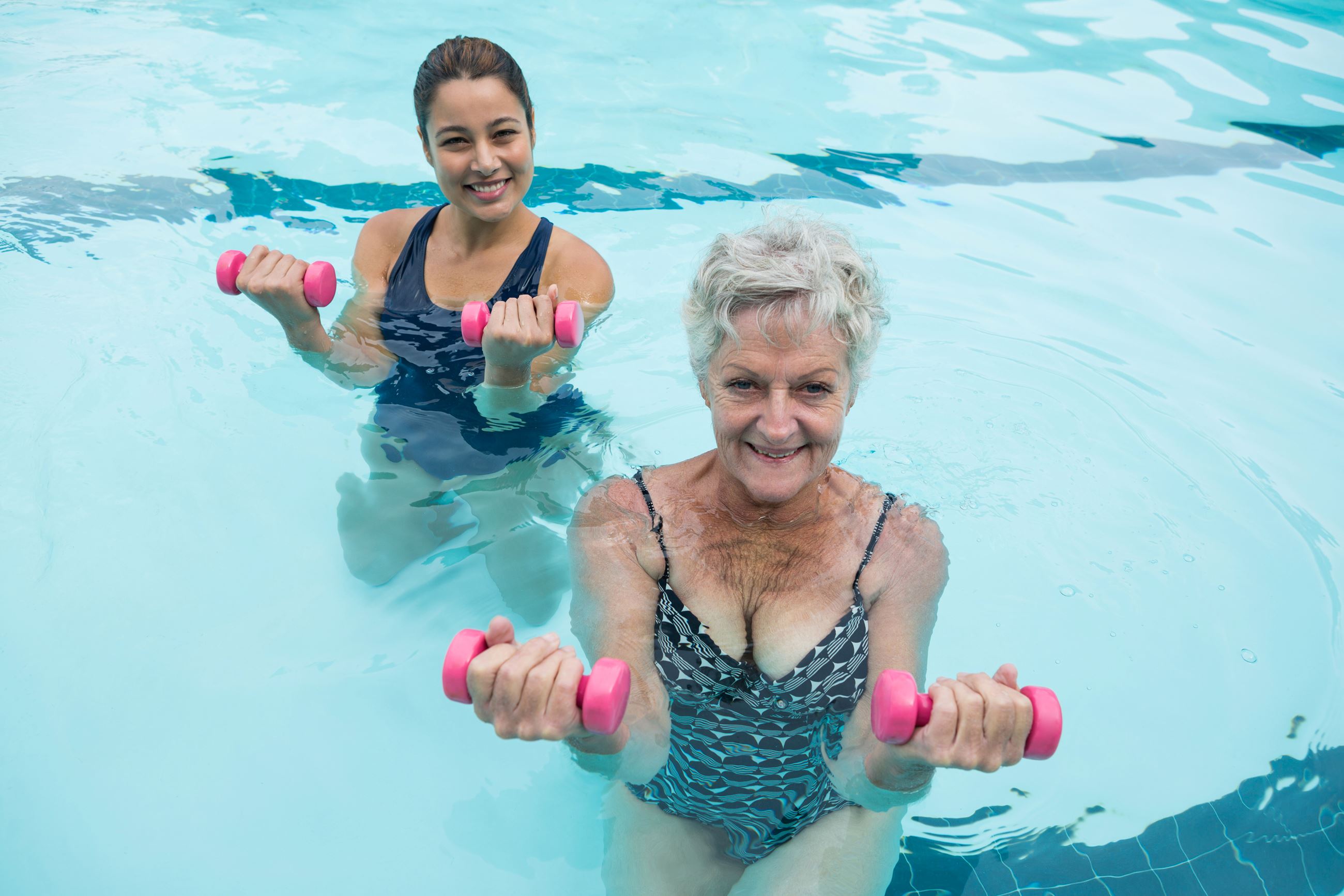 female-coach-senior-woman-exercising-with-dumbbells-swimming-pool